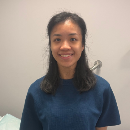 Dr Lynee Teo smiles at the camera. She is in a clinical room and is wearing a navy t-shirt
