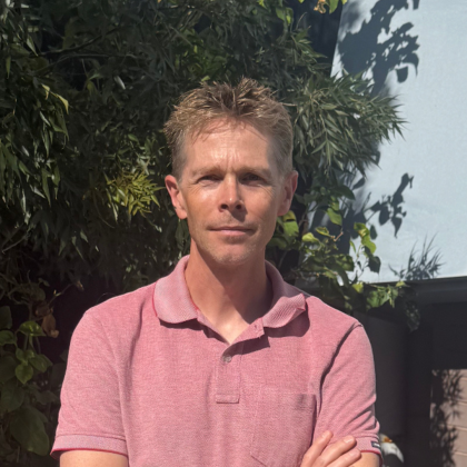 Dr Hans Bos smiles at the camera. He is wearing a short sleeve red t-shirt and has light brown short hair